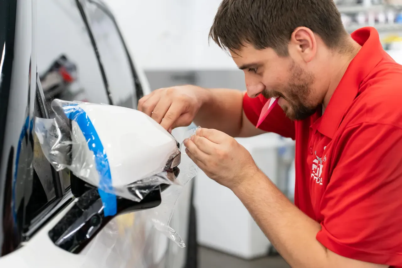 Technician carefully trimming paint protection film around a side mirror